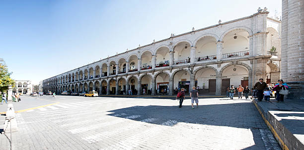 Peruvian arcade surrounding town square Arequipa, Peru - May 25, 2013: Peruvian arcade surrounding town square. Stitched panorama showing the size of the square. People are pictured walking by and cars and taxis are parked at the kerb arequipa province stock pictures, royalty-free photos & images