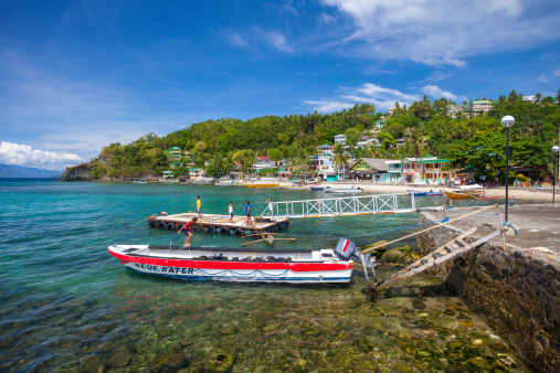 Sabang, Philippines - May 15, 2012: Small boat used for diving and snorkelling tours is mored off a Jetty. Waterside cafes and accommodation can be seen in the distance, while children are playing in the water near the boat.