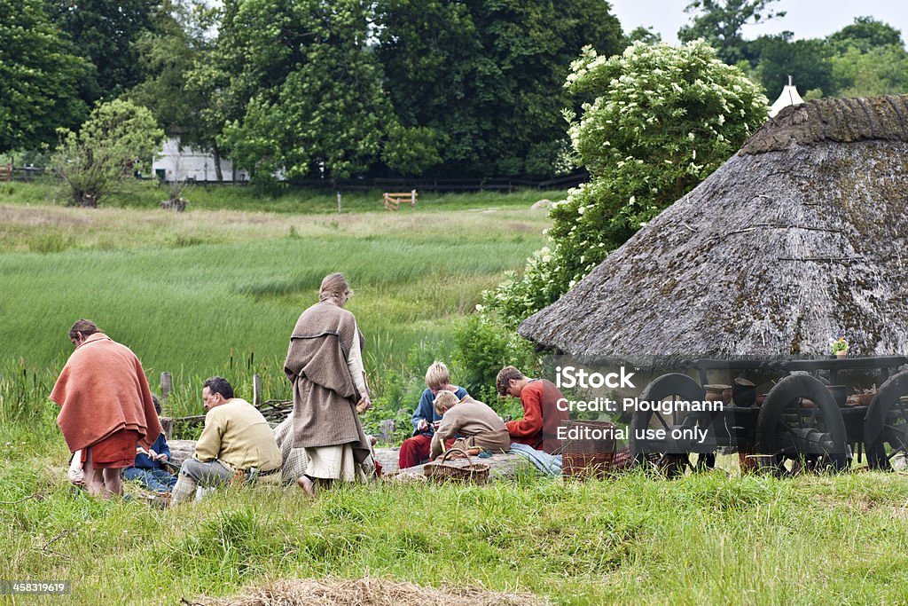 Photos from Iron Age Village, Sagnlandet Lejre, Denmark Lejre, Denmark - Juli 3, 2013 The people in the picture is part of the Sagnlandet Lejres offer to live as they did in the Iron Age in one week. Therefore, they are dressed and have tasks that you had then.A group of children and adults sitting together around a fire and eat and talk. To the right of them is an old-cart filled with kitchenware and other belongings.Behind the old carts, is an iron age hut made of clay. Its a Clay hut with thatched roof. The people live and act as they did in the Iron Age. They are dressed in authentic homespun clothes. Iron Age Stock Photo