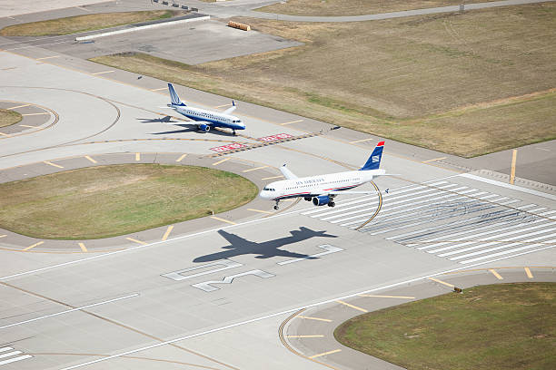 US Airways Airbus Jet Landing on Runway Minneapolis, Minnesota, USA - September 18, 2012: A US Airways Airbus A320 passenger jet (N124US) about to touchdown for landing on Runway 30 Left at the Minneapolis St. Paul International Airport (MSP). A United Express Embraer E170 (N862RW) regional jet is holding for takeoff. taxiway stock pictures, royalty-free photos & images