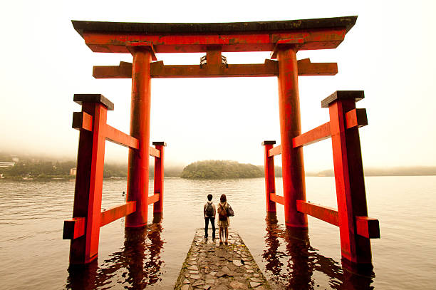 Torri Japanese gate at Hakone Lake Hakone, Japan - August 22, 2011: Two local tourists watching at the Hakone lake from a Torii (japanese gate) in a cloudy day. torri gate stock pictures, royalty-free photos & images