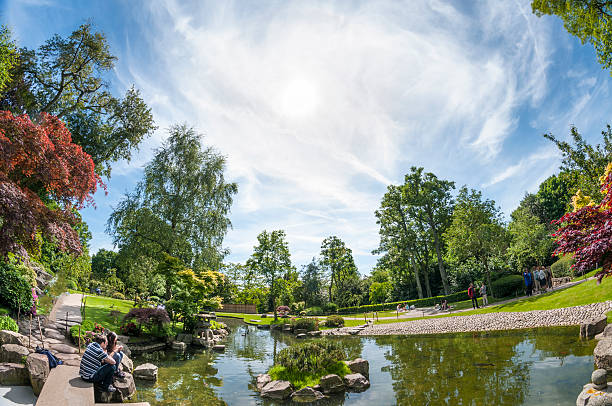 London, United Kingdom - June 4, 2013: Wide angle view of people enjoying the sun by the lake in the Oriental Gardens in Holland Park, London, England