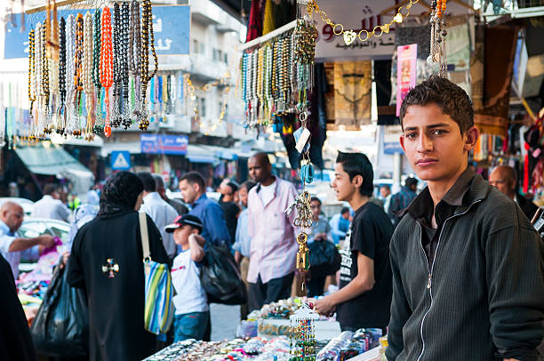 Amman, Jordan - November 8, 2010: A Jordanian teenager (foreground) stands outside the shop where he works in the busy commercial center of Amman.