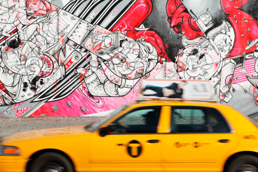 New York, NY, USA: December 6, 2012: A yellow taxi cab speeds west in a blur of motion along Houston Street on the Lower East Side of Manhattan past the Bowery Mural Wall. The mural wall features a changing array of street art works. The one on display here is \