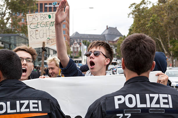 Protests against NPD election campaign Wiesbaden, Germany - August 26, 2013: Young counterprotestor, screaming and shouting against a NPD election campaign speech in the city center of Wiesbaden. Founded in 1964 the NPD is a German nationalist party, its agitation is racist, antisemitic and revisionist. In the foreground a police cordon - trying to separate the nazis from the protestors national democratic party of germany stock pictures, royalty-free photos & images