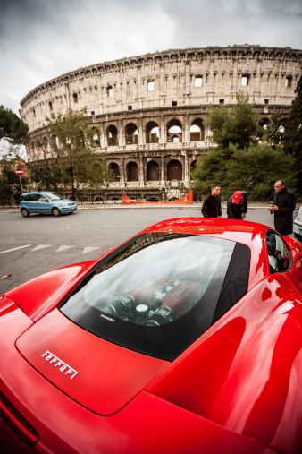 Rome, Italy - December 16, 2012: A red Ferrari 458 Italia parked just in front of the Coliseum in Rome, with people passing by and admiring the super expensive sport car