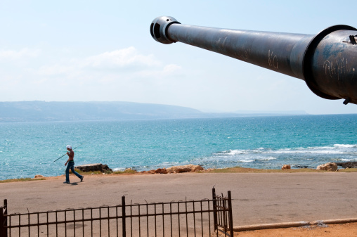 Tripoli, Lebanon - September 8, 2010: A Lebanese man with a fishing pole walks past an old decommissioned artillery piece on the coast. The word 