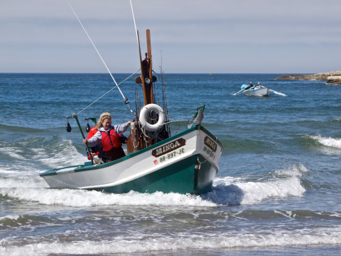 Pacific City, Oregon, USA - July 21, 2013:  A Dory boat and passengers returning to the beach at Cape Kiwanda located in Pacific City, Oregon. A Double-end Rowing Dory can be seen in the distance. Returning from fishing these boats will be loaded onto a boat trailer on the sandy beach.