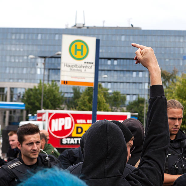 Protests against NPD election campaign Wiesbaden, Germany - August 26, 2013: Counterprotestors against a NPD election campaign speech in the city center of Wiesbaden - giving the finger towards the NPD truck. In the background a riot police cordon trying to separate Nazis and protestors from each other. Founded in 1964 the NPD is a German nationalist party, its agitation is racist, antisemitic and revisionist. national democratic party of germany stock pictures, royalty-free photos & images