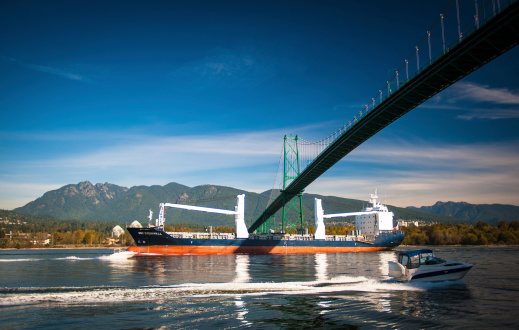 Vancouver, Canada - October 8, 2012: An oil tanker or bulk cargo shipping vessel passes under the Lion's Gate Bridge on the Burrard Inlet in Vancouver, British Columbia, while a recreational vessel passes in the opposite direction. If approved, oil pipeline expansion projects would involve a dramatic increase of tanker traffic in the area.