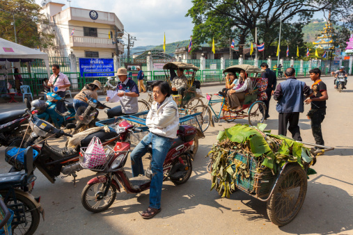 Mae Sai, Thailand - December 13, 2011: Motorcycles, riders and some rickshaws makes their way towards the border checkpoint at Mae Sai on the border between Thailand an Myanmar. The border area is busy with trade between the two countries.