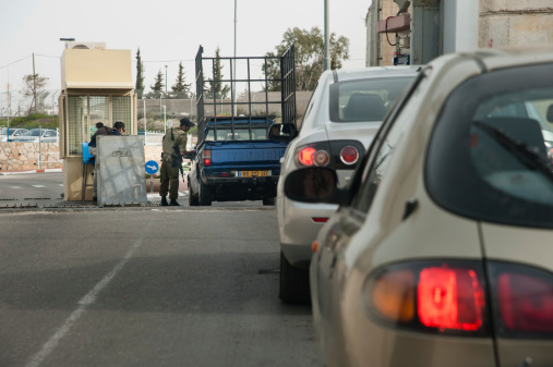 Betlehem, Palestinian Territory - March 3, 2013: A soldier checks cars passing through the Israeli military checkpoint controlling movement between Bethlehem and Jerusalem through the separation wall, March 3, 2013.