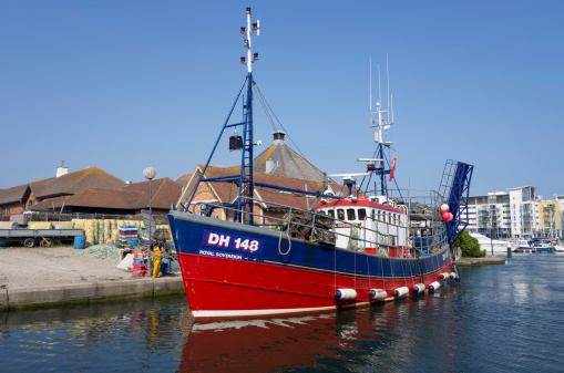 Eastbourne, UK - July 7, 2013: The location is the Sovereign Harbour Marina, on the South Coast of England at the seaside resort of Eastbourne in Sussex. Boats are arriving back after a days sailing watched by tourists and visitors. Part of the marina is set aside for fishing boats and trawlers. These have come from the sea back to their moorings in the late afternoon on a hot sunny summers day in July to unload their catch. They take advantage of the good weather to fulfil their fish quotas.