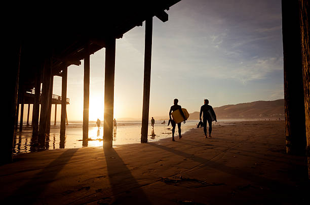 Surfistas ao pôr do sol em Pismo Beach, Califórnia - foto de acervo