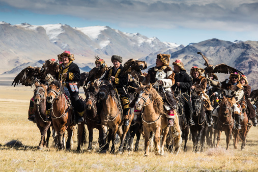 Sagsay, Mongolia - September 22, 2012: Mongolian eagle hunters riding to the festival. A group of mongolian eagle hunter  from Kazakh tribe is riding to the eagle hunter festival of Sagsay with their  golden eagles on the arm. They wear their  traditional skin clothes, which are typical for western Mongolia, Altai area.Kazakh people in  the western part of mongolia domesticate female golden eagles for hunting. By this eagles they are hunting hare, foxes and even wolves during the very cold winter time.