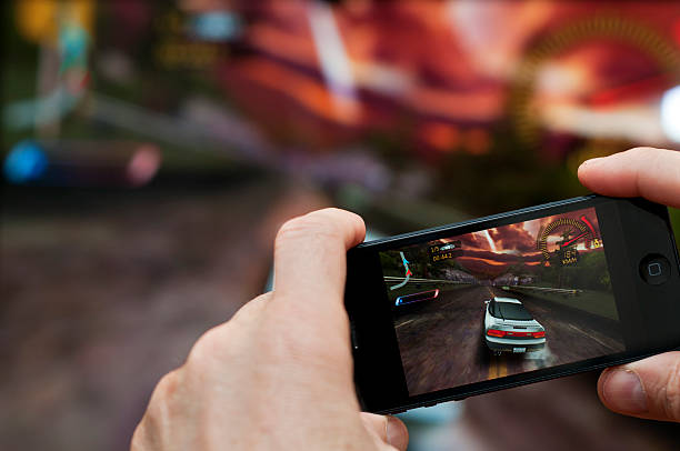 Bad Oeynhausen, Germany - December 30, 2012: Man playing a car racing game on an iPhone 5. View on his hands, holding the mobile phone in front of a big display. The iPhone is connected to the TV via WLAN with an Apple TV.