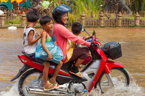 Siem Reap, Cambodia - October 18, 2011: Woman drives through floodwaters in the town of Siem Reap, Cambodia on a scooter with three children as passengers onboard.