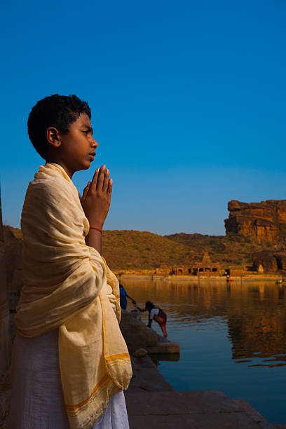 Badami, India - February 23, 2009: A young boy Brahmin priest leads a small group prayer at the reservoir edge near the Bhutanatha group of cave temples on February 23, 2009 in Badami, India