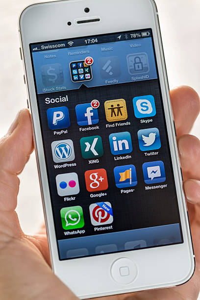 Apple iPhone 5, Social folder Geneva, Switzerland - April 6, 2013: A woman's hand holding an iPhone 5. Close-up shot of her hand and the iPhone on showing a folder called "Social". The Smartphone is produced by Apple Computer, Inc. pinterest stock pictures, royalty-free photos & images