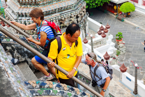 Bangkok, Thailand - February, 18th 2013: Tourists are walking upstaits temple Wat Arun in Bangkok, old landmark of town. In capture an Asian man is walking down and a caucasian couple is walking upstairs.