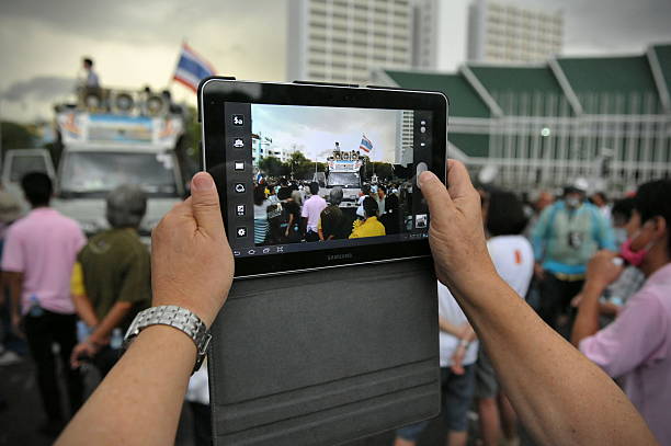 Anti-Government Rally in Bangkok Bangkok, Thailand - November 24, 2012: A protester uses a tablet computer to photograph a rally on Makhawan Bridge organised by the nationalist Pitak Siam group. Pitak Siam are calling for the government to be overthrown. peoples alliance for democracy stock pictures, royalty-free photos & images