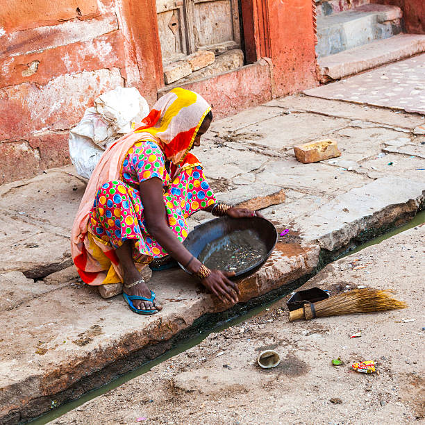 Bikaner, India - October 24, 2012: An Indian woman is working as a road sweeper. She is screening the open sewers for silverdust, as there are many silversmiths in this part of town.