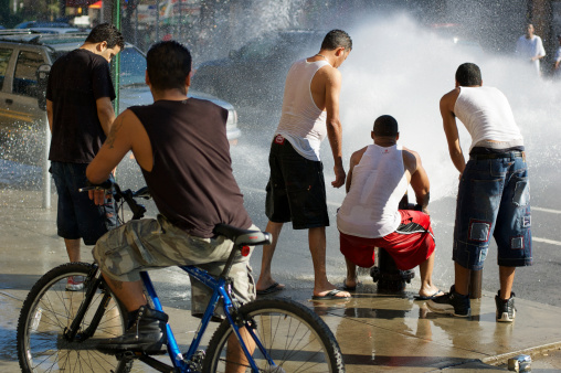New York City, USA - July 16, 2006: Group of young men gather at an open fire hydrant in upper Manhattan. The fact that tampering with fire hydrants is illegal does not stop people from opening them on hot summer days.
