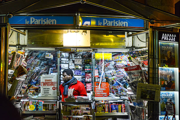 Paris, France - December 26, 2012: Newsstand in Paris at night. Black vendor rearranging newspapers and magazines inside the kiosk