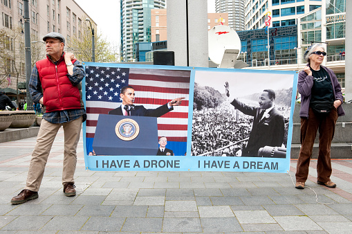 Seattle, USA - April 17, 2013: A man and woman at West Lake Park holding a banner of President Obama and Martin Luther King protesting the use of military drones.