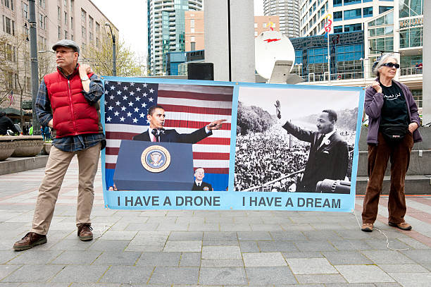 Military Drone Protest Seattle, USA - April 17, 2013: A man and woman at West Lake Park holding a banner of President Obama and Martin Luther King protesting the use of military drones. air attack photos stock pictures, royalty-free photos & images