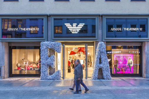 Munich, Germany - December 13, 2012: People strolling in front of the Emporio Armani store in Theatinerstrasse. The shop windows are decorated for Christmas.