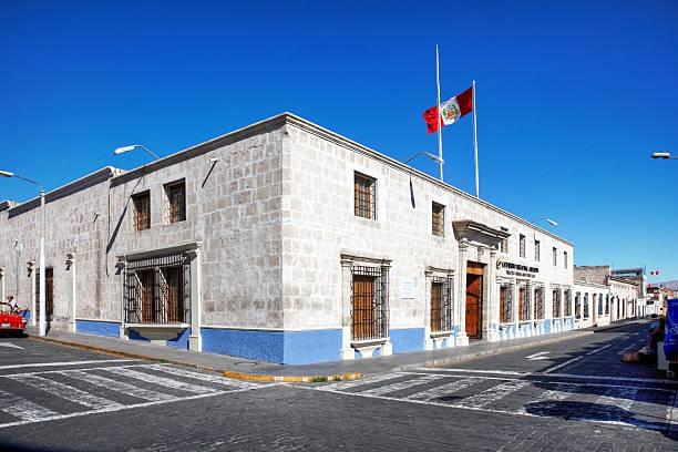 Arequipa, Peru - May 25, 2013: Peruvian arcitecture building on corner of cobblestoned street in the city of Arequipa. People are pictured preparing a red vintage car for a wedding is parked at the kerb
