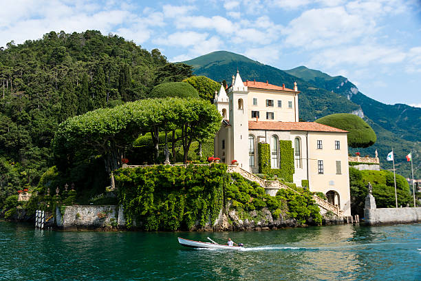 Man driving boat in front of lake side villa -XXXL Lenno, Italy - July 1, 2013: A man driving a small boat in front of  the Villa Balbianello on Lake Como.  The villa was built in the 1500's and is located on the tip of a small peninsula on the western shore of the lake. lake como photos stock pictures, royalty-free photos & images