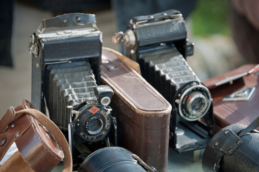 Brugine, Italy - March 3, 2013: Old bellows cameras and original binocular and lens leather cases on the table of a flea market stall. Shot in Brugine (Padua province, Italy) during the monthly flea market.