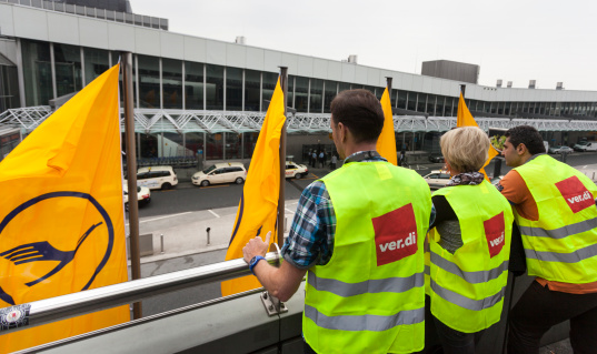 Frankfurt, Germany - April 22, 2013: Ground staff of Lufthansa entered into a one-day token strike. Members of german trade union verdi with yellow reflective vests are looking at Terminal 1, Airport Frankfurt, in the background some flags of Lufthansa.