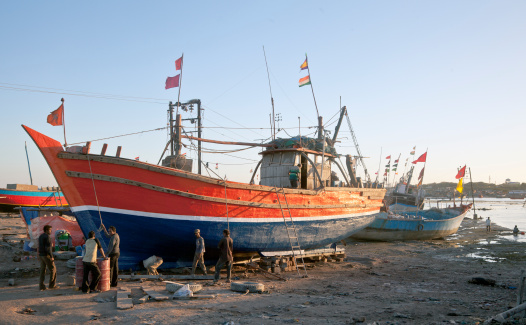 Gujarat, India - February 27, 2013: Landscape at the estuary of boatyard where a repair crew are in discussion on the next strategy of a repair job