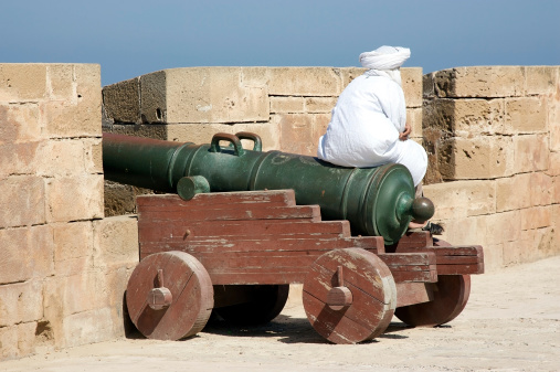 Essaouira, Morocco - September 13, 2012: african man of the berber ethnic group is sitting on the cannon at the fortified walls of the Essaouira.