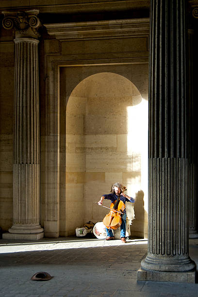 Paris, France - September 19, 2013: Man playing his cello for money at one of the entrance of the Louvre museum. With more than 8 million visitors each year, the Louvre is the world's most visited museum. Photo taken in Paris, France, on September 19, 2013.