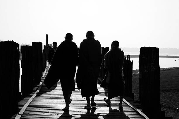 Monks and People Traveling on U Bein Bridge Amarapura, Myanmar - January 15, 2011 Burmese monks and people traveling on U Bein Bridge. U Bein Bridge was built in 1849 with a total of 1086 teak wood posts and 482 teak wood spans. The bridge is 1.2 km long across the shallow Taungthaman lake in Amarapura. black and white travel travel destinations monk stock pictures, royalty-free photos & images