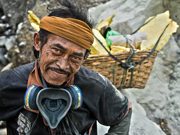 Java, Indonesia - May 25, 2013: Sulfur miner posing in front of basket loaded with solid sulfur at the Kawah Ijen volcano in East Java, Indonesia.