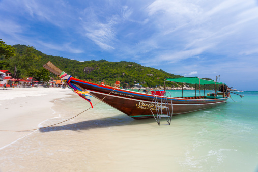Surat Thani, Thailand - September 30, 2011: A colourful long tail boat is on the Haad Rin Beach Ko Phangan, Thailand during the daytime. People can be seen on the beach in the background and in the water.