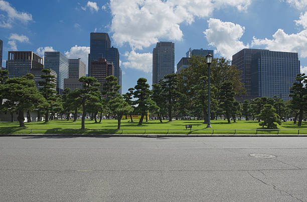 Tokyo, Japan - October 8, 2013: Sidewalk, small park (with lawn and Japanese Black Pine trees), people, street with motor vehicles and skyscrapers in Central Tokyo on a sunny morning.