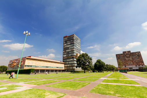 Mexico City, Mexico - July 24, 2013: Central University Campus of the Mexico National Autonomous University, a UNESCO World Heritage Site. The Central Campus constitute a unique and outstanding example of the application of the 20 century modernism style merged with the pre-hispanic Mexican tradition. A one of the most significant icons of modern urbanism and architecture in the country and the region. View of the Rectorate Tower and Central Library from the architecture faculty with students passing by.