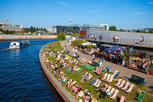 Berlin, Germany - June 27, 2011: High angle view over a riverside bar next to the river Spree in central Berlin as a passenger boat passes by. Many people can be seen on deck chairs enjoying the weather.