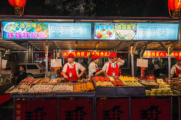 Beijing fast food stall in colourful night market China Beijing, China - 27th September 2013: Cooks grilling and selling traditional street food from a sidewalk stall in a vibrant night market in the heart of downtown Beijing, China. wangfujing stock pictures, royalty-free photos & images