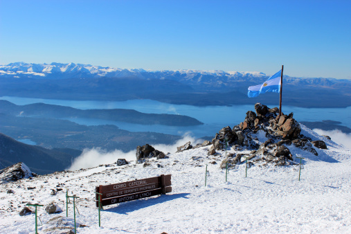 San Carlos de Bariloche, Cerro Catedral, Argentina - July 18, 2013: Argentina Flag and Gutierrez lake at Andes - Patagonia 2Argentina flag stand at the top of CERRO CATEDRAL MOUNTAIN - in front of Lynch Refuge (Patagonia - Argentina).The Refugio Lynch or Lynch Refuge is a little building located at the top of the CERRO CATEDRAL mountain and was built on 1943.GutiArrez Lake (Spanish: Lago GutiArrez) is a lake of the lake region of northern Patagonia, in Argentina. This lake has 16,4km2 and is connected to Nahuel Huapi Lake.CERRO CATEDRAL is a mountain located near San Carlos de Bariloche, within Nahuel Huapi National Park - Argentina. This mountain has one of the main SKI Resorts of South America, with 600 hectares of skiable surface divided into 53 well sign-posted trails of various difficulties, which reach 2.000 meters over sea level.