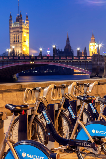 London, UK - February 11, 2012: London - A Barclays cycle hire point with The Palace of Westminster in the background at dusk.