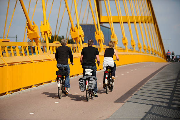 Utrecht, the Netherlands - August 5, 2011: Three people cycling on Hogeweidebrug in Utrecht. Focus is on the man in the middle. At the background more cyclists can be seen. There is a sidewalk for pedestrians on the right side.The yellow Hogeweidebrug over the Amsterdam-Rhine canal connects the city of Utrecht with Leidsche Rijn. In june 2008 the bridge opened to traffic. Leidsche Rijn is a new neighbourhood of Utrecht, located west of the existing city.