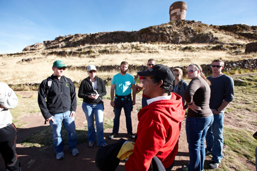 Sillustani, Peru - May 28, 2013: A chullpa is an ancient Aymara funerary tower originally constructed for a noble person or noble family. Chullpas are found across the Altiplano in Peru and Bolivia. The tallest are about 12 metres (39 ft) high. A group of tourists listen to an explanation from their Peruvian guide
