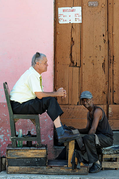 Trinidad, Cuba - Januari 3, 2011:A poor shoe shiner in a street of Trinidad polishes shoes of a prosperous Cuban official. Trinidad is a pitoresque town in the province of Sancti SpA-ritus, central Cuba. UNESCO declared Trinidad to be a part of world cultural heritage in 1988.